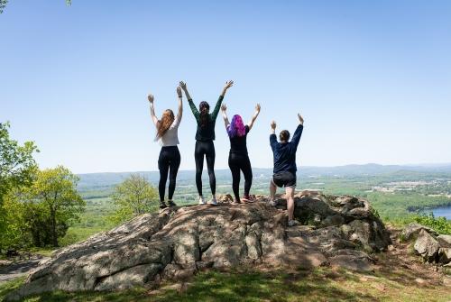 四名高年级学生在霍利奥克山山顶高举双臂欢呼